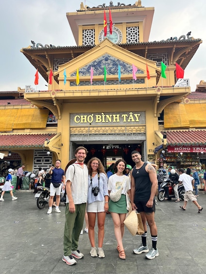 A group of people standing in front of a building with a sign that reads "CHO BÌNH TÂY". 1