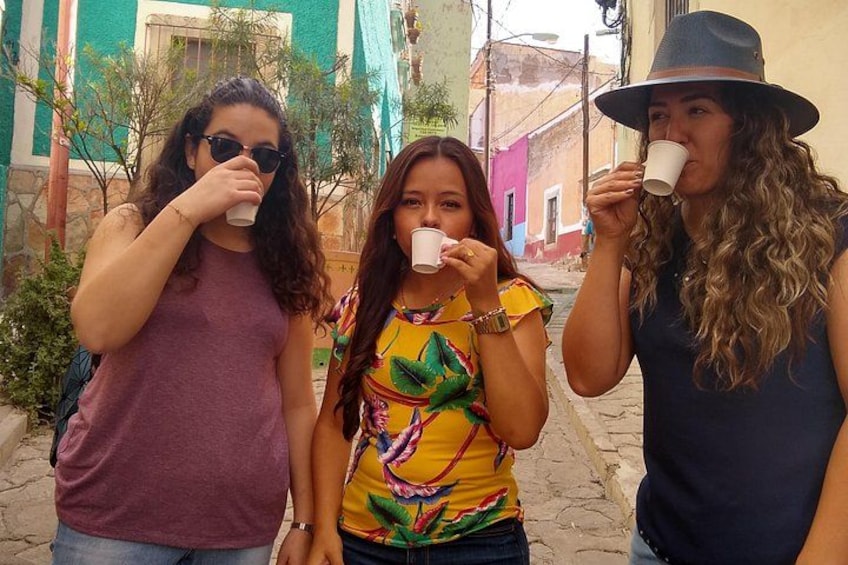 Three people drinking from white cups in a narrow street with colorful buildings. 5