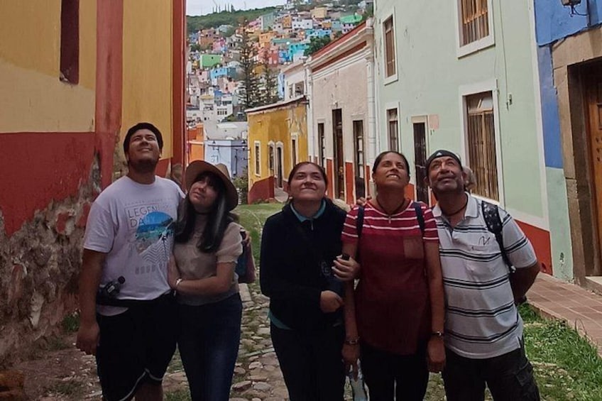 A group of people standing on a cobblestone street in a colorful neighborhood with buildings in pastel colors. 3