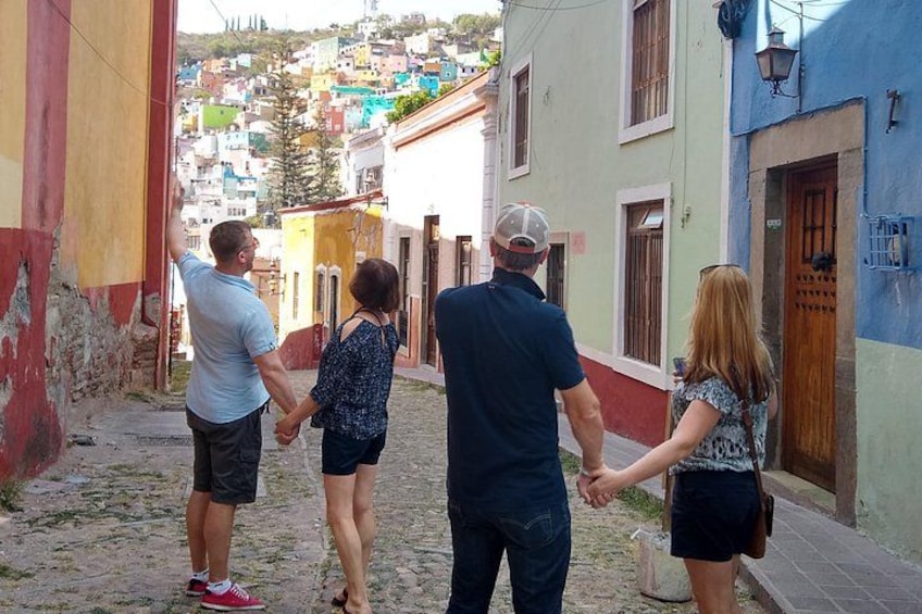 A group of people walking down a narrow street with colorful buildings on either side. 4