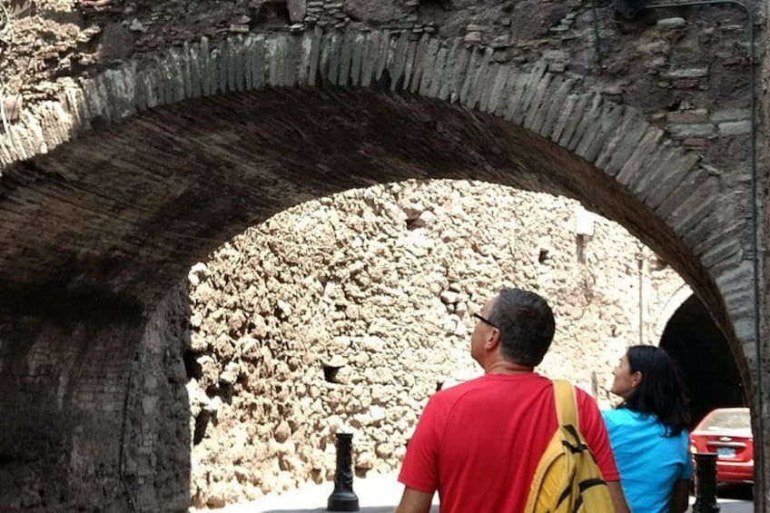 An ancient stone archway with tourists observing the interior. 1