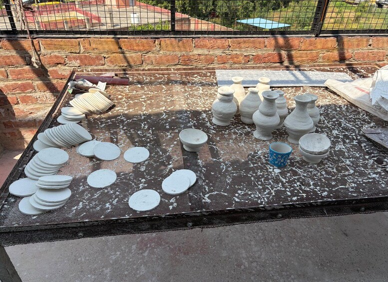 Objetos de cerámica sobre una mesa al aire libre, incluyendo platos, cuencos y jarrones. 5