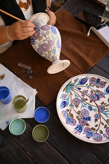 Une personne est en train de peindre une assiette en céramique avec des motifs floraux. 1