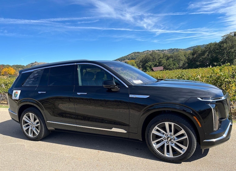 A black SUV parked on a road with a clear sky and hills in the background. 1