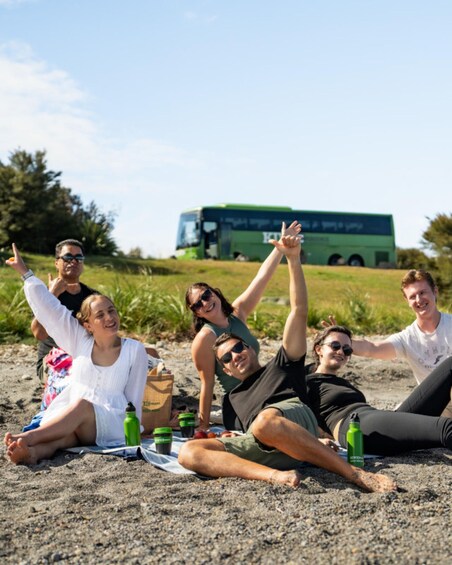 A group of people relaxing on a sandy beach with a green bus in the background. 1
