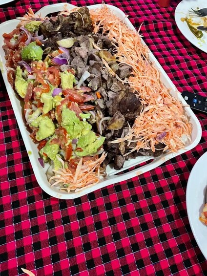 A tray of food with shredded carrots, meat, and a green salad on a red and black checkered tablecloth. 2