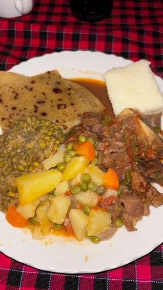 A plate of food with meat, potatoes, peas, carrots, and a side of flatbread. 3