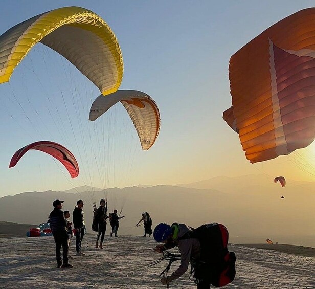 A group of people preparing for paragliding on a mountain with large parachutes. 1