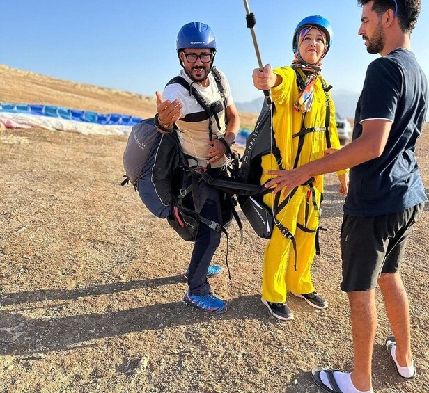 Three people wearing helmets and harnesses, standing on a dirt ground with a clear sky in the background. 3