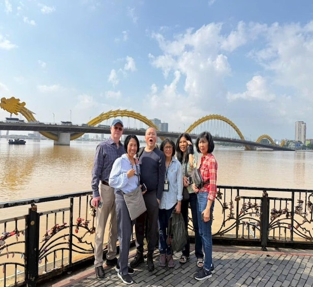 A group of people standing on a bridge with a river and a distinctive yellow arch bridge in the background. 2