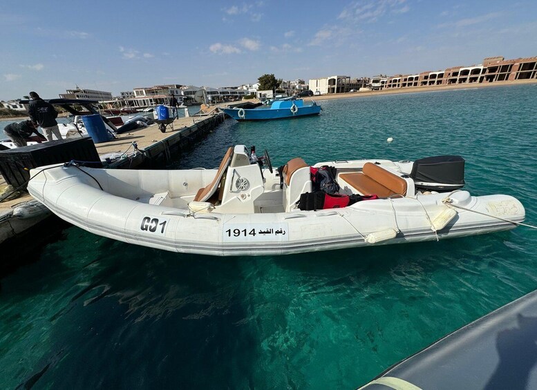 A white inflatable boat with the number 1914 on its side, docked at a marina with other boats and buildings in the background. 3