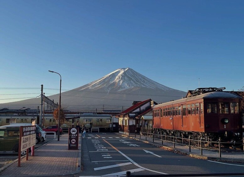 A train station with a red train, a platform, and a snow-capped mountain in the background. 1