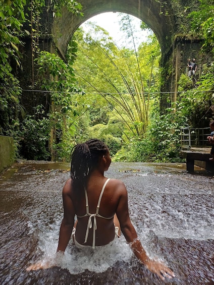 A person in a white bikini standing in a water body with a stone bridge overhead. 1