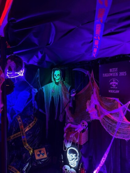 A Halloween-themed decoration with a figure in a hooded cloak, a neon skull, and a sign for 'REJSY HALLOWEEN 2025'. 5