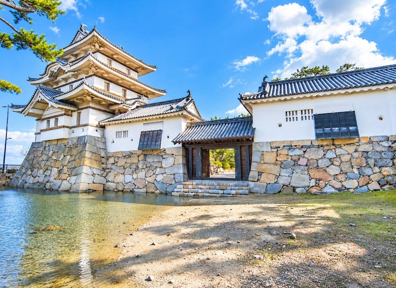 A traditional Japanese castle with multiple tiers and a stone base, surrounded by a calm lake and clear skies. 4