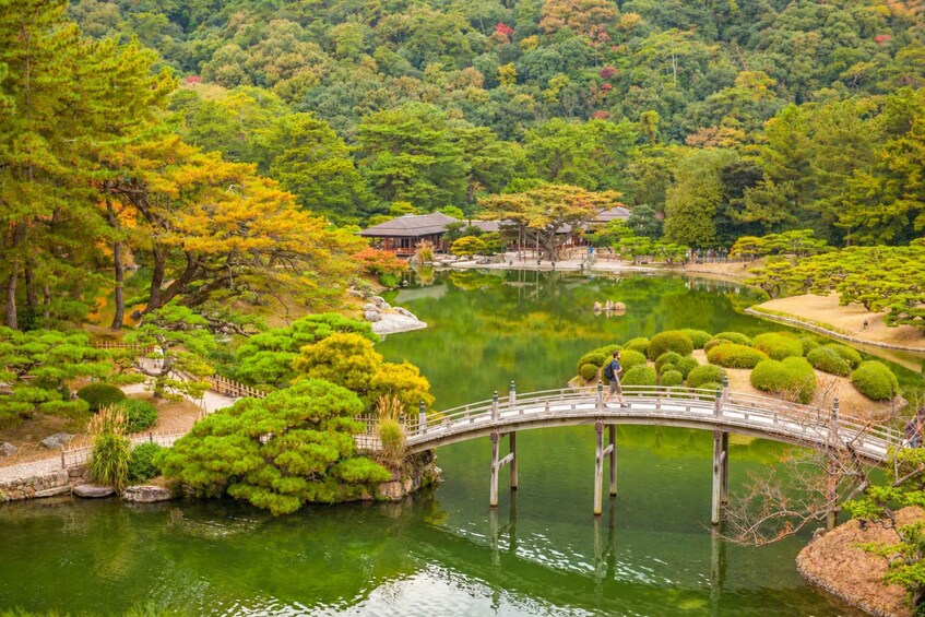 A traditional Japanese garden with a wooden bridge over a pond, surrounded by lush greenery and a mountainous backdrop. 2