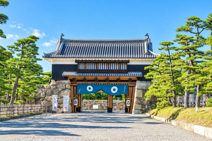 A traditional Japanese gate with a tiled roof, stone walls, and a blue banner with a white circle. 3
