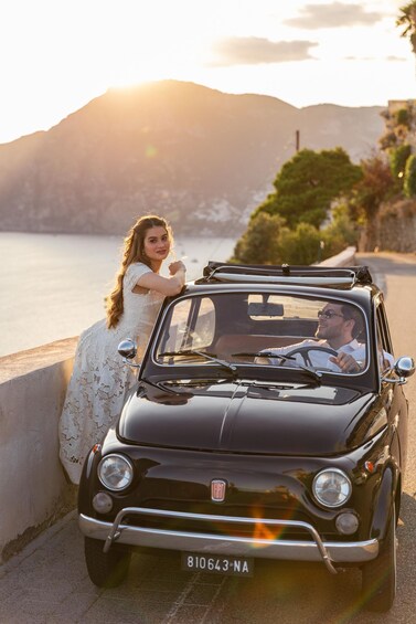 A vintage car parked by a scenic lakeside with mountains in the background. 1