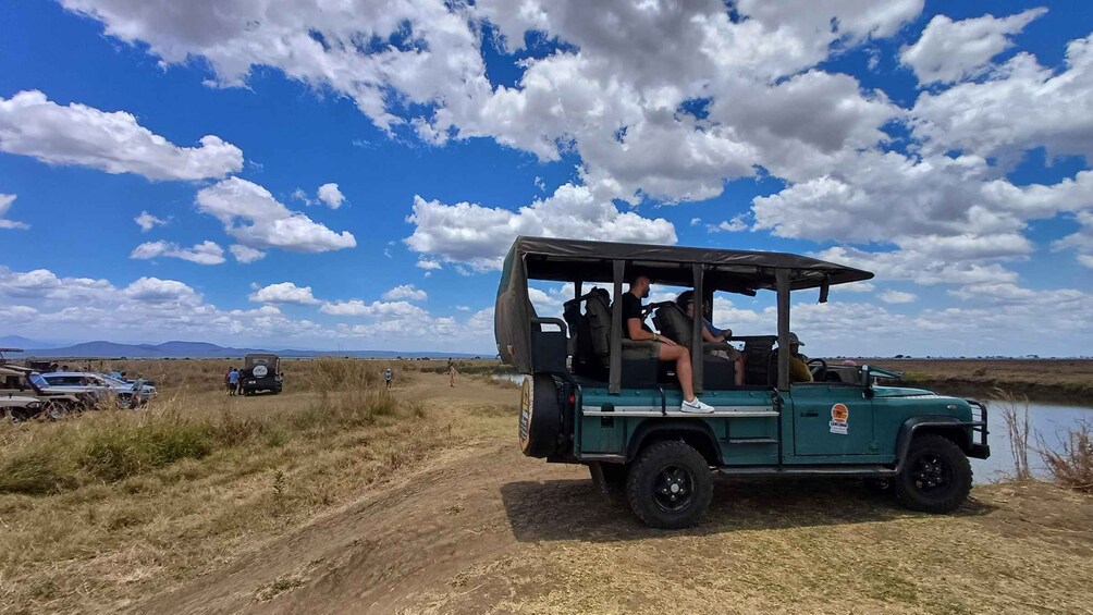 A green safari vehicle parked on a dirt path with a lake and mountains in the background. 2
