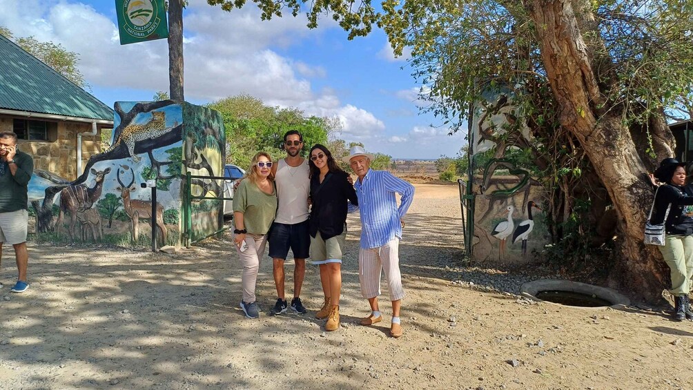 A group of people posing in front of a wildlife mural at a park entrance. 1