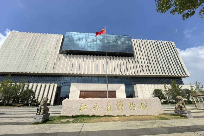 A modern building with a flag, stone statues, and a stone plaque with Chinese characters. 1