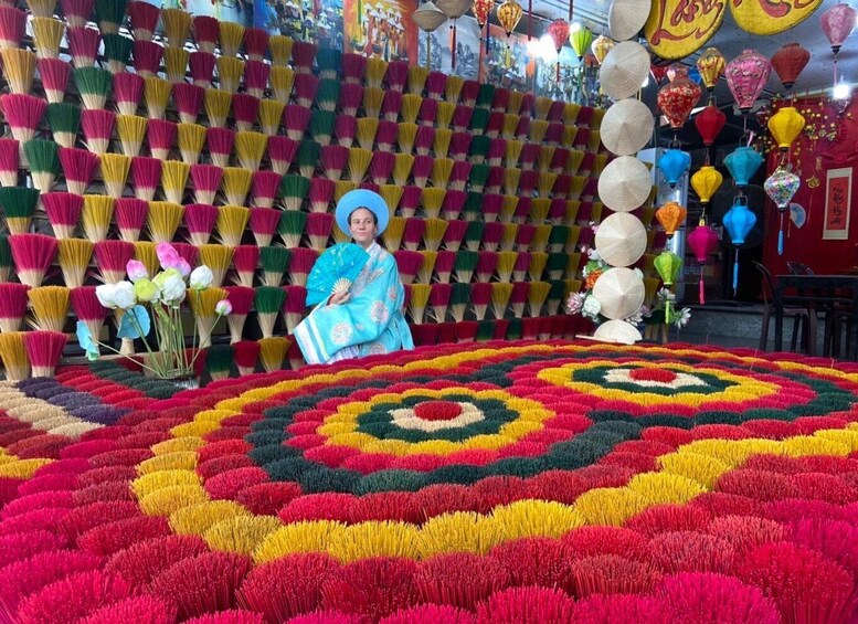 A person in traditional attire holding a fan, surrounded by vibrant, colorful flower arrangements and decorative lanterns. 5