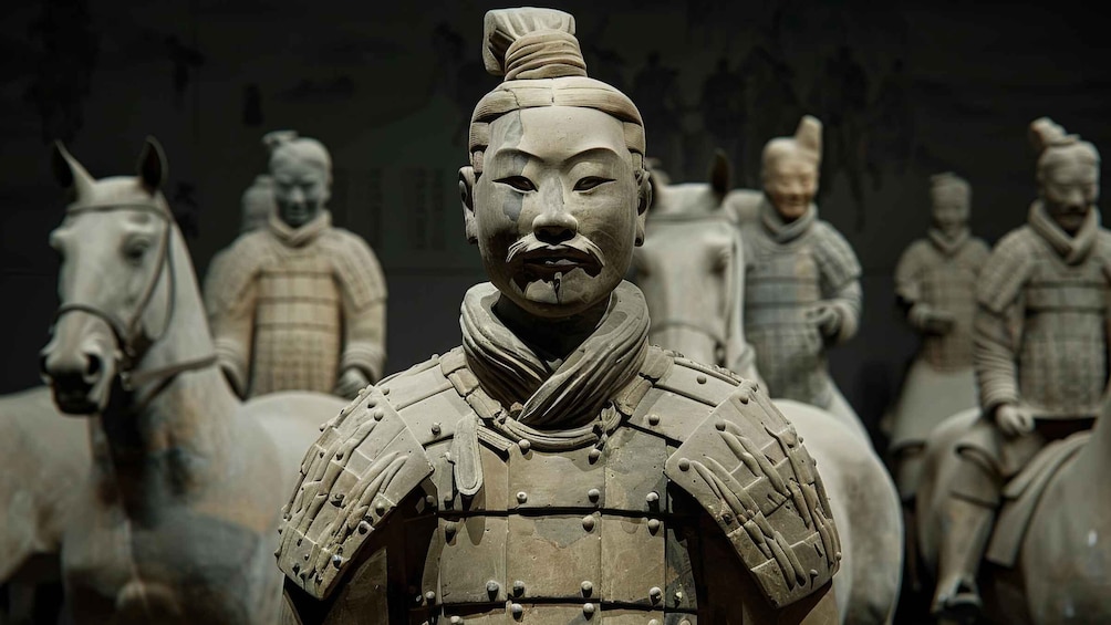 A terracotta statue of a warrior in armor with a horse, surrounded by other similar statues. 1
