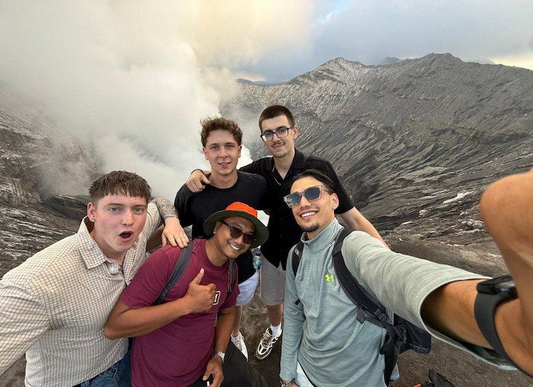 A group of people taking a selfie on a mountain with a rocky landscape and clouds in the background. 3