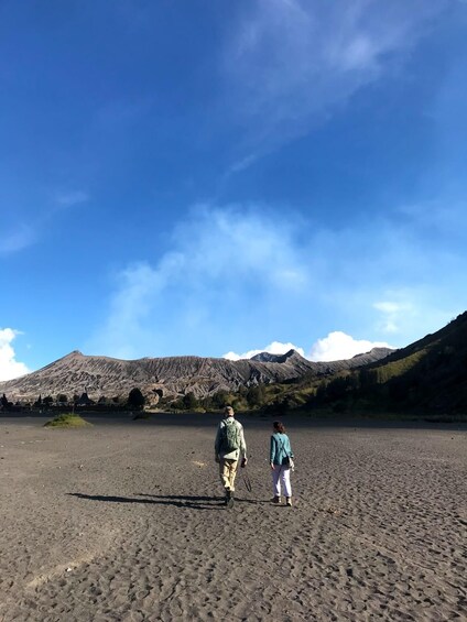 Two people walking on a beach with mountains in the background. 2