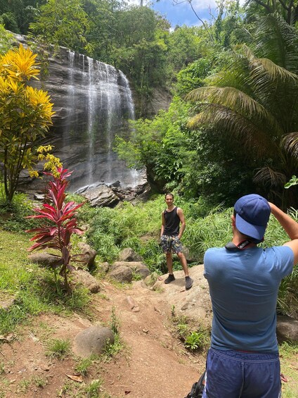 A waterfall in a lush, green forest with a person taking a photo. 2