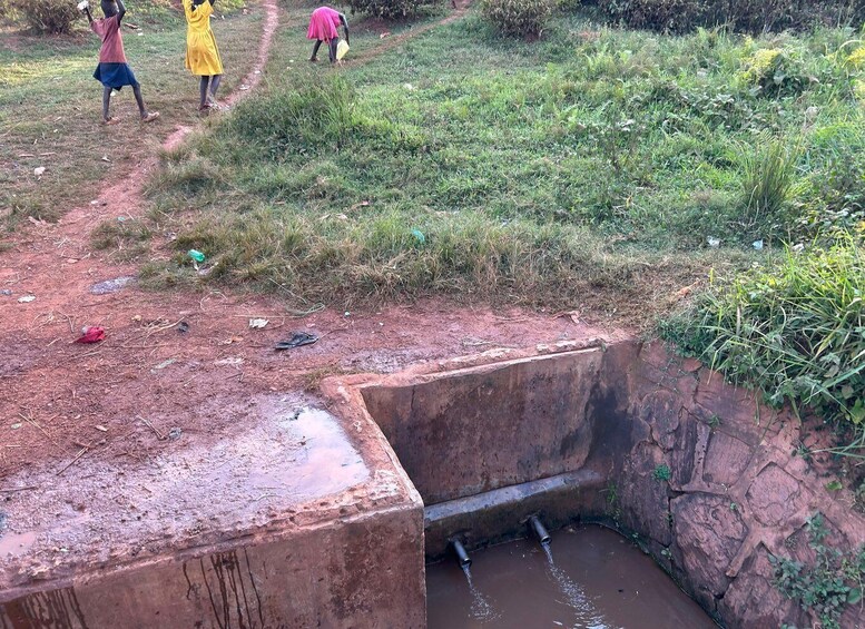 A muddy pit with water flowing into it, surrounded by a grassy area with a dirt path. 3