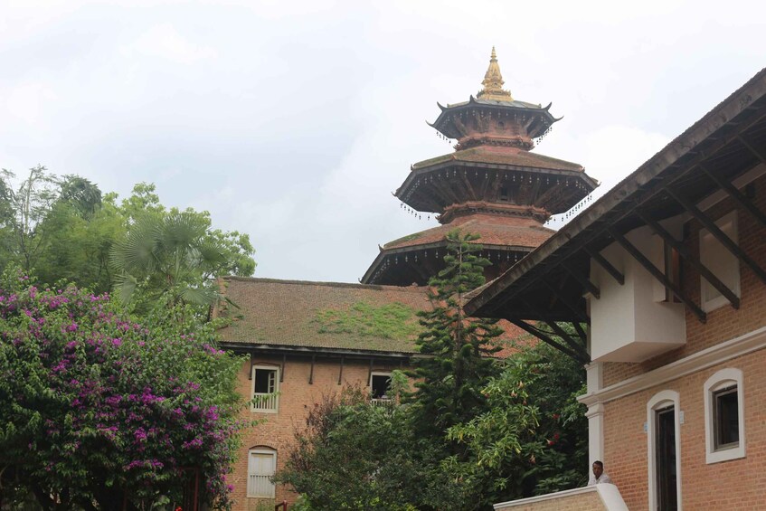 En traditionell, flervånings pagoda med en gyllene spira, omgiven av frodig grönska och en byggnad i tegel med en balkong. 2