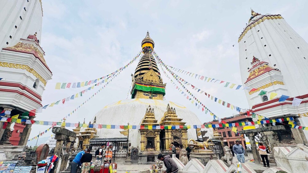 En stor stupa omgiven av mindre byggnader och människor, och prydd med färgstarka böneflaggor. 4
