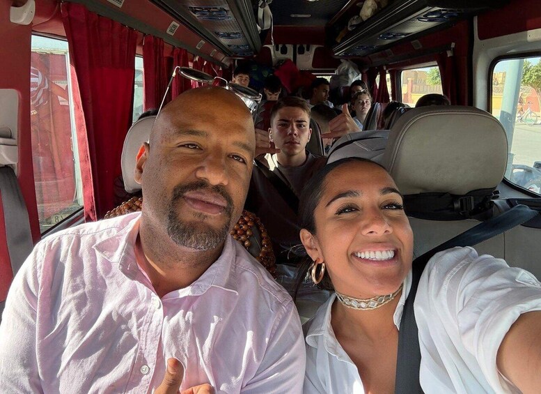 A group of people inside a bus with red curtains and a window showing a building outside. 1