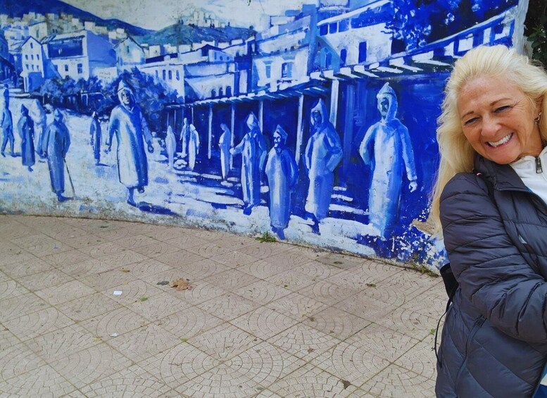 A person standing in front of a mural depicting a street scene with buildings and people. 3