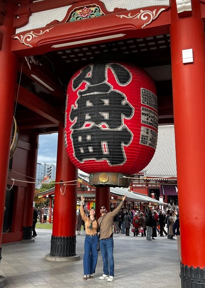 A couple posing under a large red lantern with Chinese characters, surrounded by traditional architecture and a crowd of people. 1