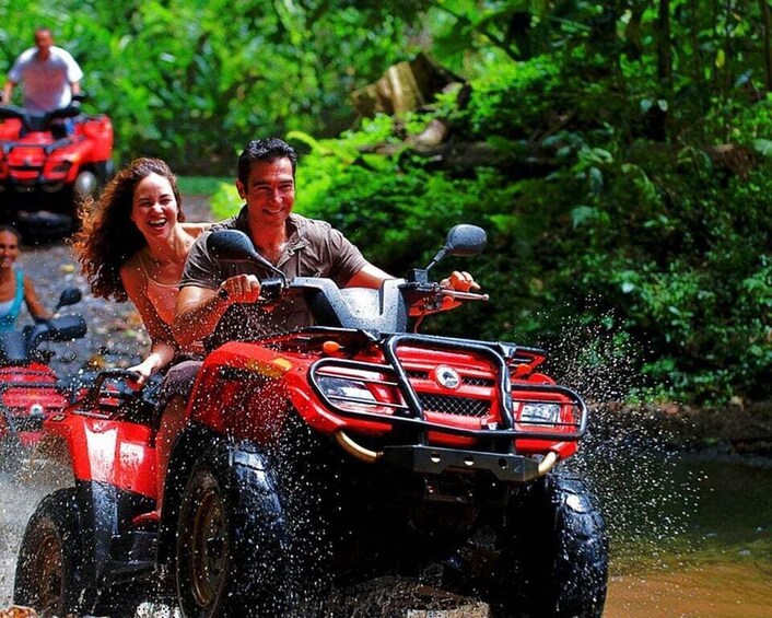A red ATV with two people, splashing through water. 2