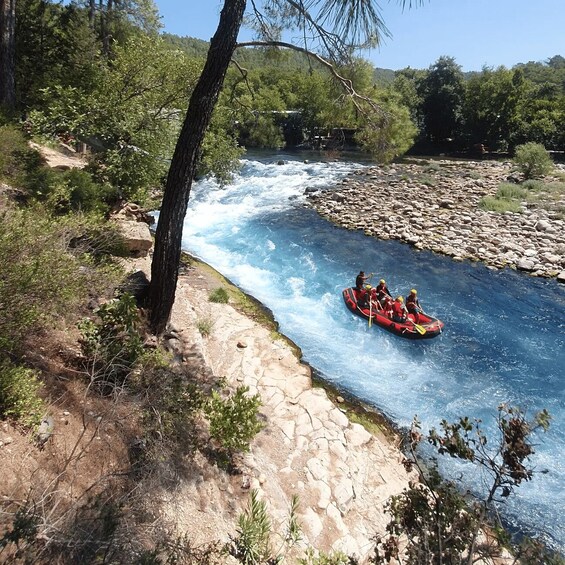 A group of people rafting down a river surrounded by rocky terrain and trees. 4