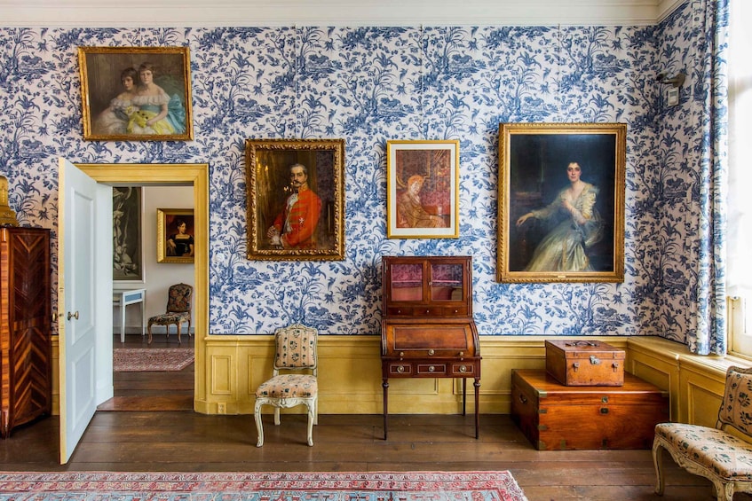 A room with floral wallpaper, wooden furniture, and framed portraits. 4