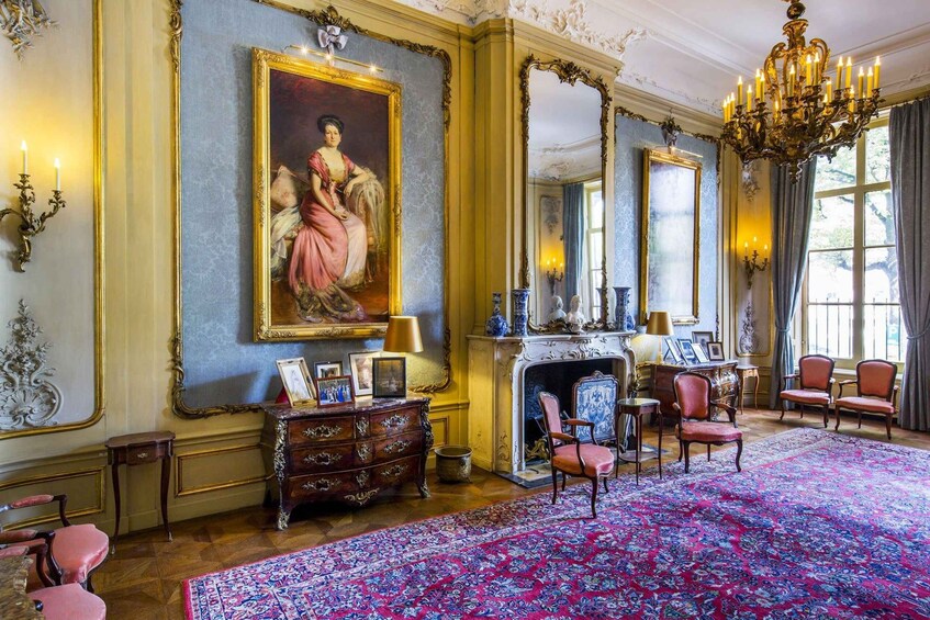 A grand room with ornate decorations, a large painting, a fireplace, and several chairs. 3