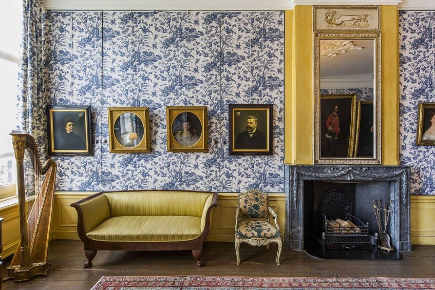 A room with blue and white floral wallpaper, a yellow sofa, a chair, a harp, and a fireplace. 2