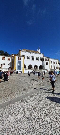 A cobblestone plaza with a white building with yellow trim and arches. 2