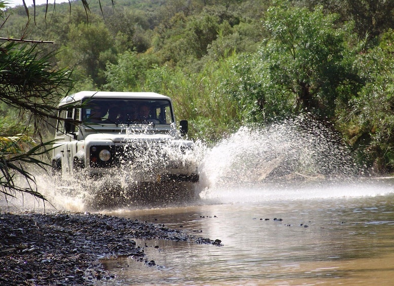 A vehicle driving through a shallow water crossing, splashing water around. 1