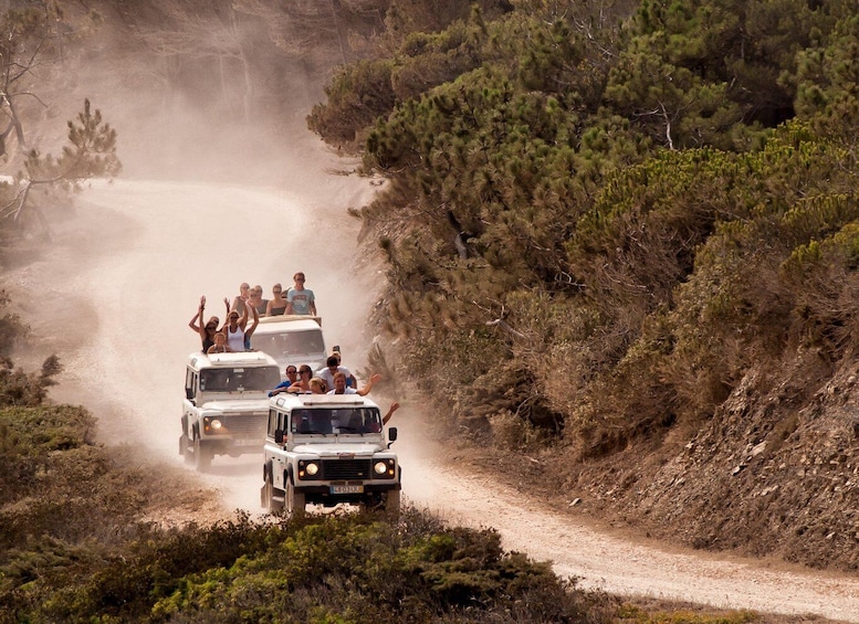 A convoy of off-road vehicles on a dusty road surrounded by sparse vegetation. 2