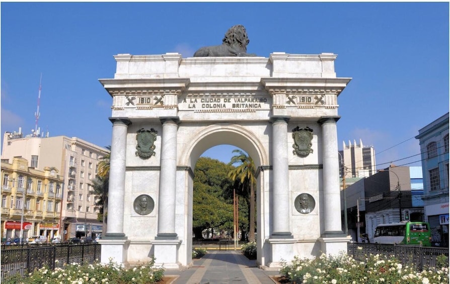 A large stone archway with a lion statue on top, surrounded by flowers and palm trees. 1
