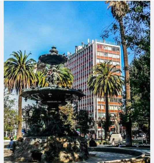 A fountain with statues, palm trees, and a tall building in the background. 2