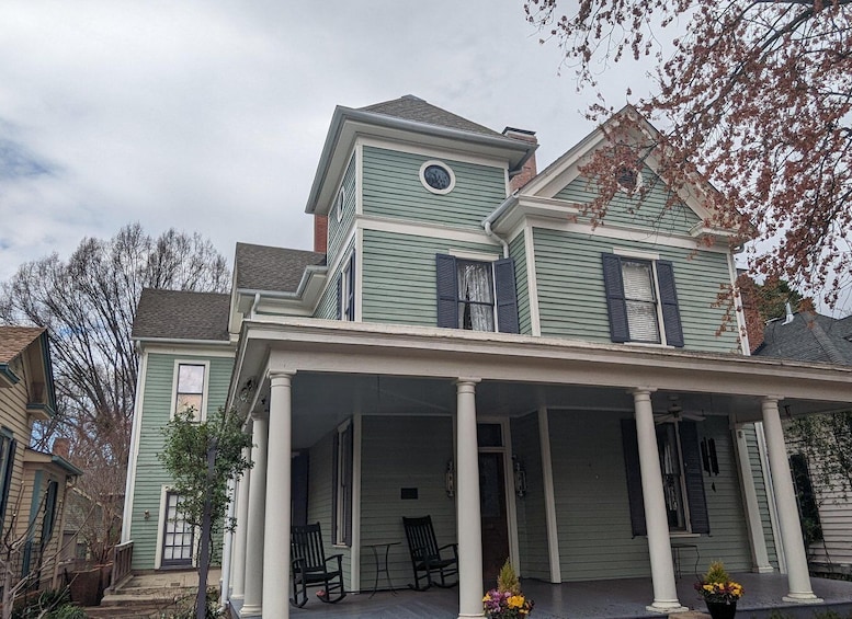 A large, green Victorian-style house with a wrap-around porch and multiple chimneys. 1