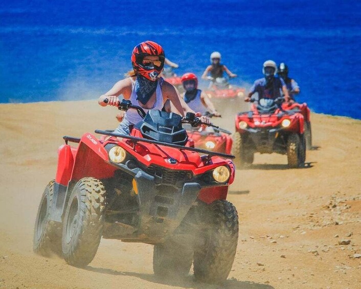 People riding red ATVs on a sandy beach with the ocean in the background. 1