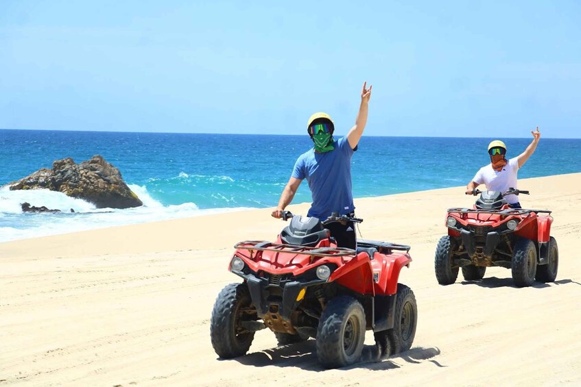 Two people riding red ATVs on a sandy beach with the ocean in the background. 3