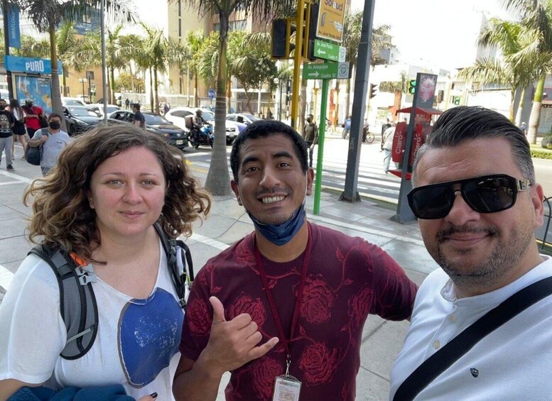 Three people posing on a city street with palm trees and cars in the background. 5